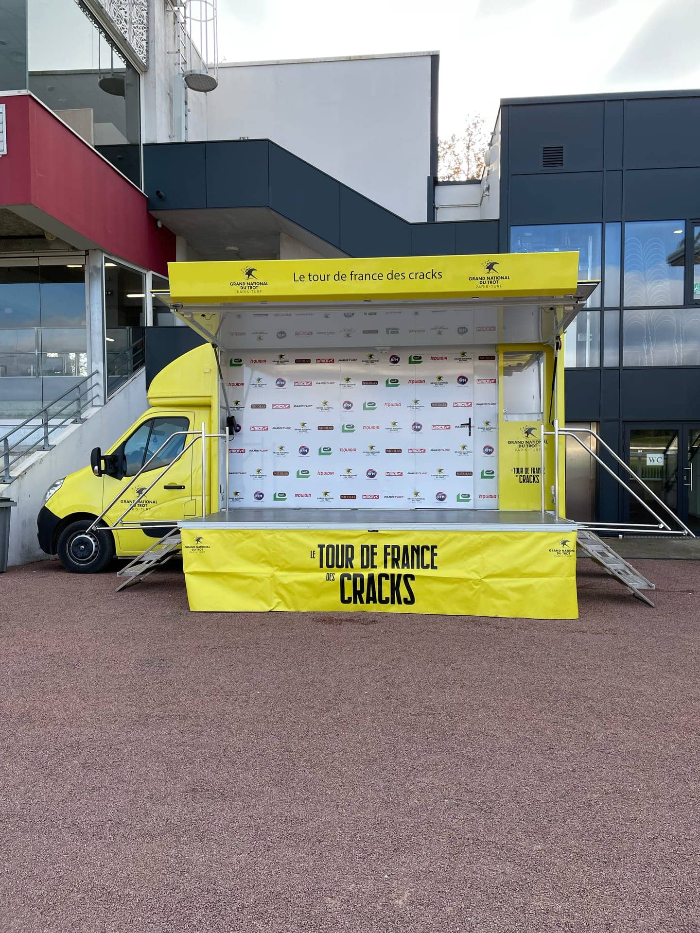 Camion podium Grand National du Trot - scène jaune ouverte avec backdrop partenaires et escaliers d'accès