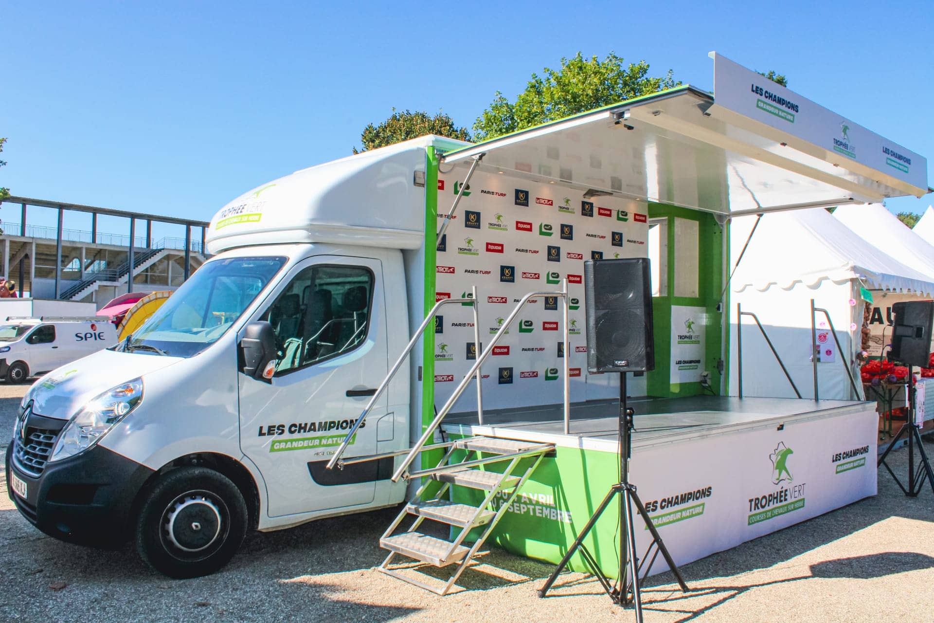 Camion podium Trophée Vert - scène déployée avec mur de partenaires et sonorisation sur pieds
