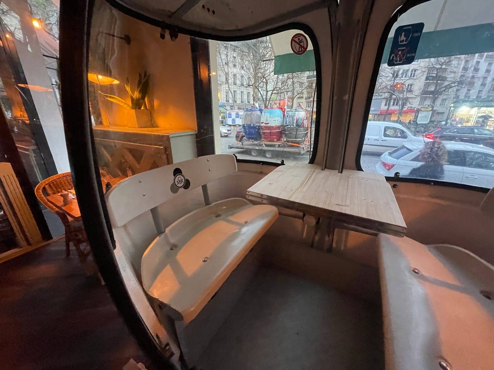 Intérieur d'une télécabine Megg avec ses banquettes d'origine et sa tablette rabattable, face à une avenue parisienne