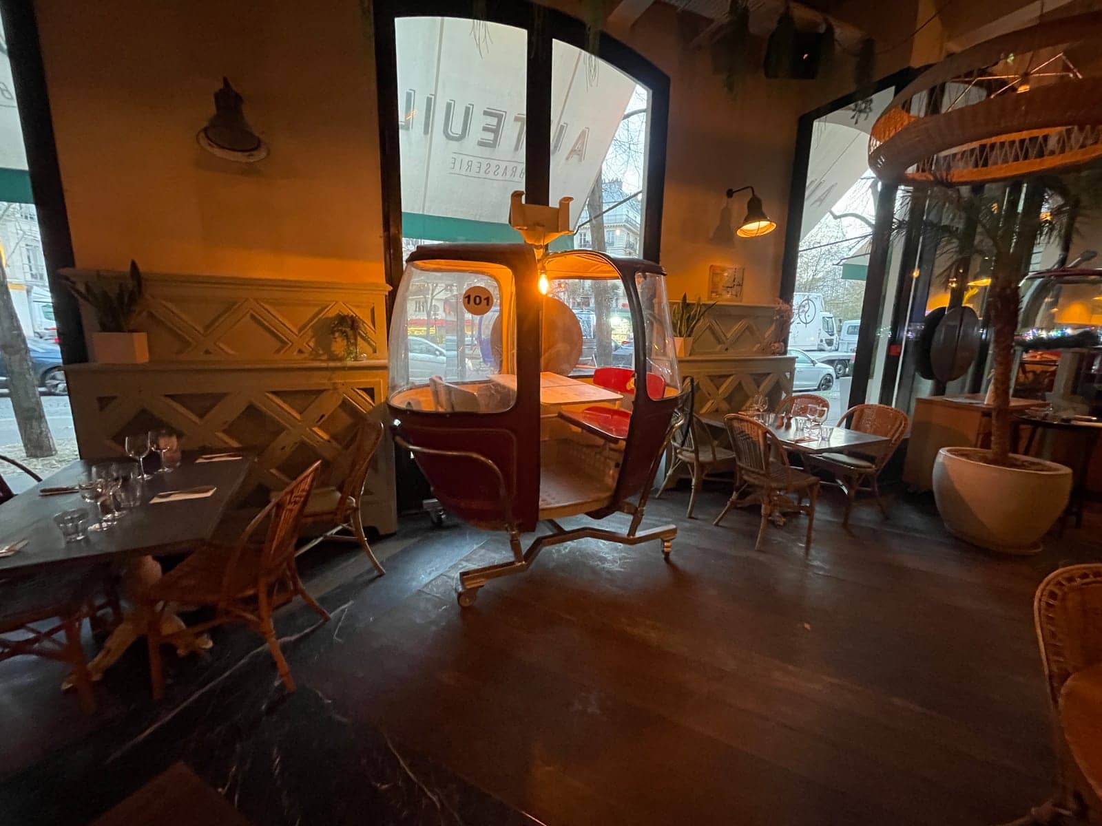 Télécabine Megg posée entre les tables de la brasserie Auteuil, sous l'enseigne de l'établissement
