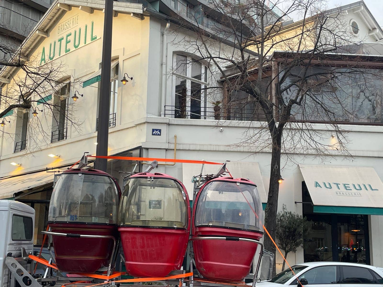 Trois télécabines Megg sanglées sur une remorque, livrées devant la brasserie Auteuil à Paris