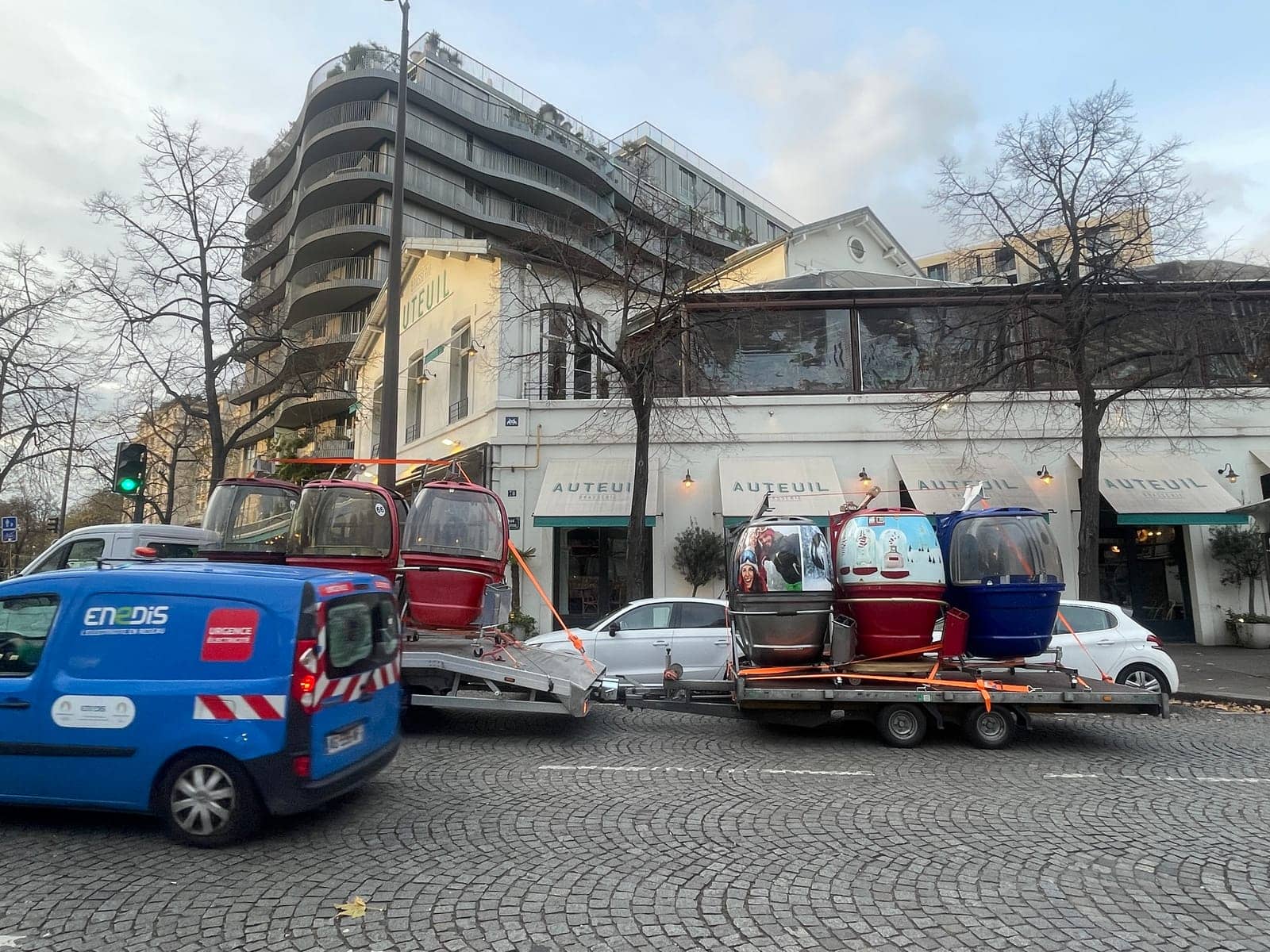 Remorque chargée de télécabines Megg circulant dans une rue parisienne, entre voitures et immeubles