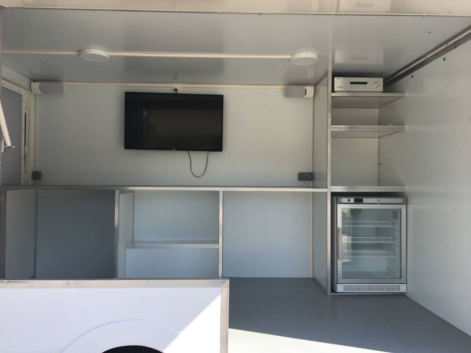 Intérieur du camion podium Nike avec écran plat mural, réfrigérateur vitré et rangements modulables blancs