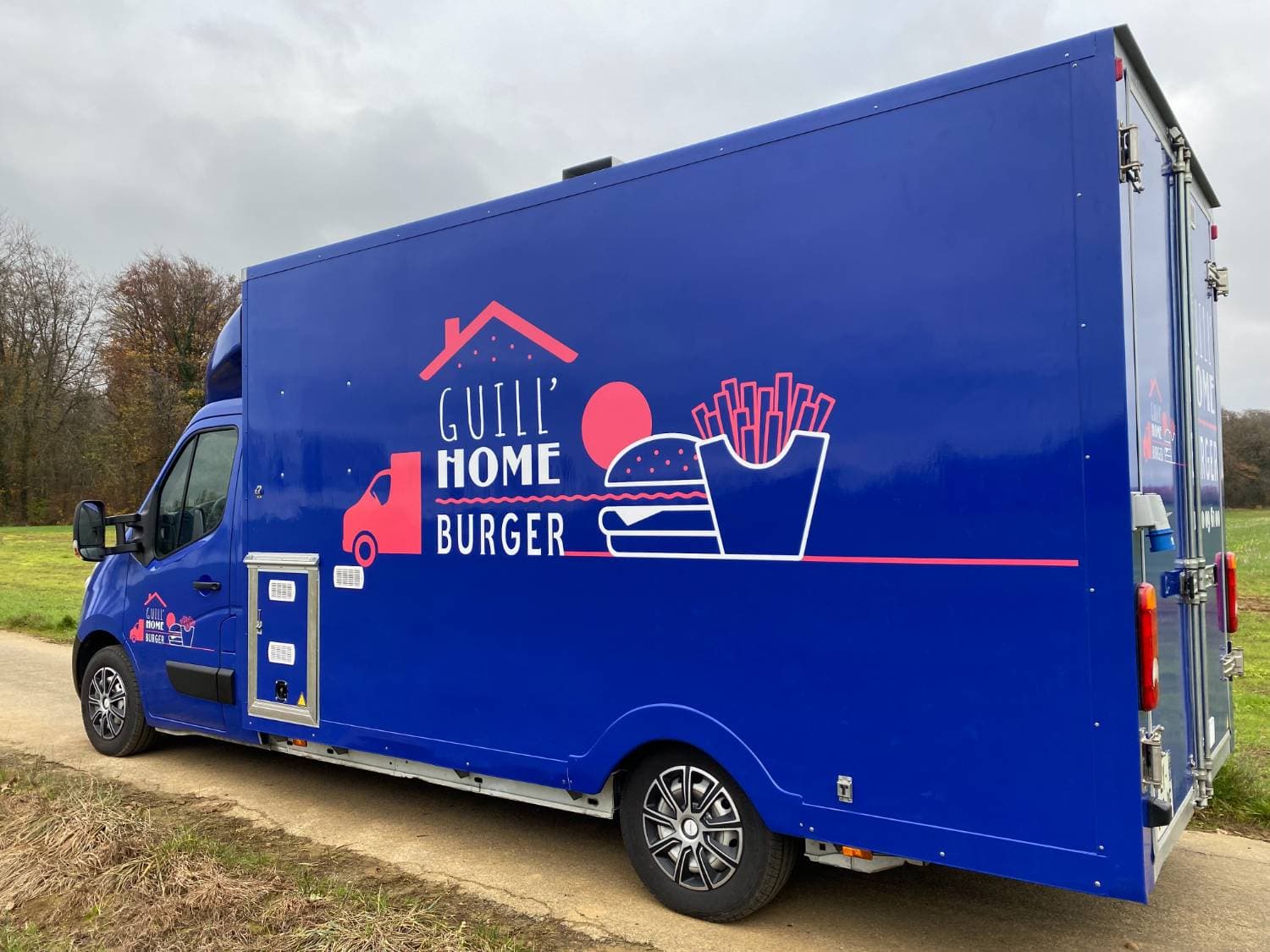 Vue arrière food truck Guill'Home Burger bleu avec grand logo burger et frites sur covering latéral