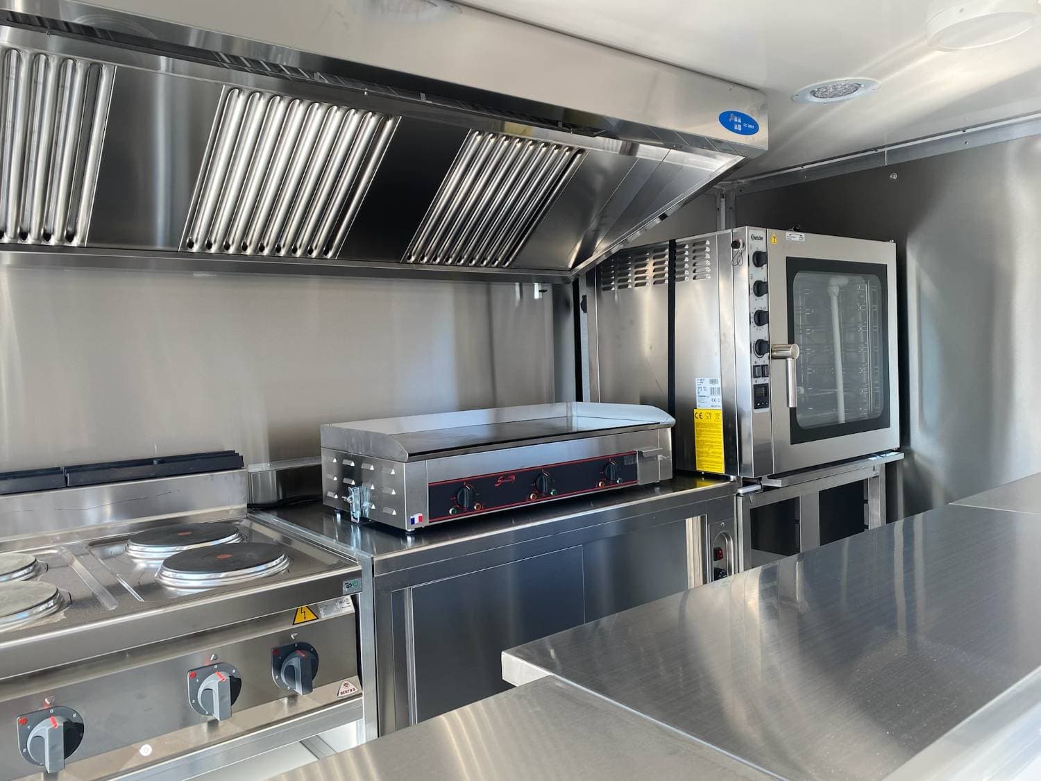 Intérieur cuisine professionnelle avec plancha, four à convection, plaques électriques, hotte et plan de travail inox