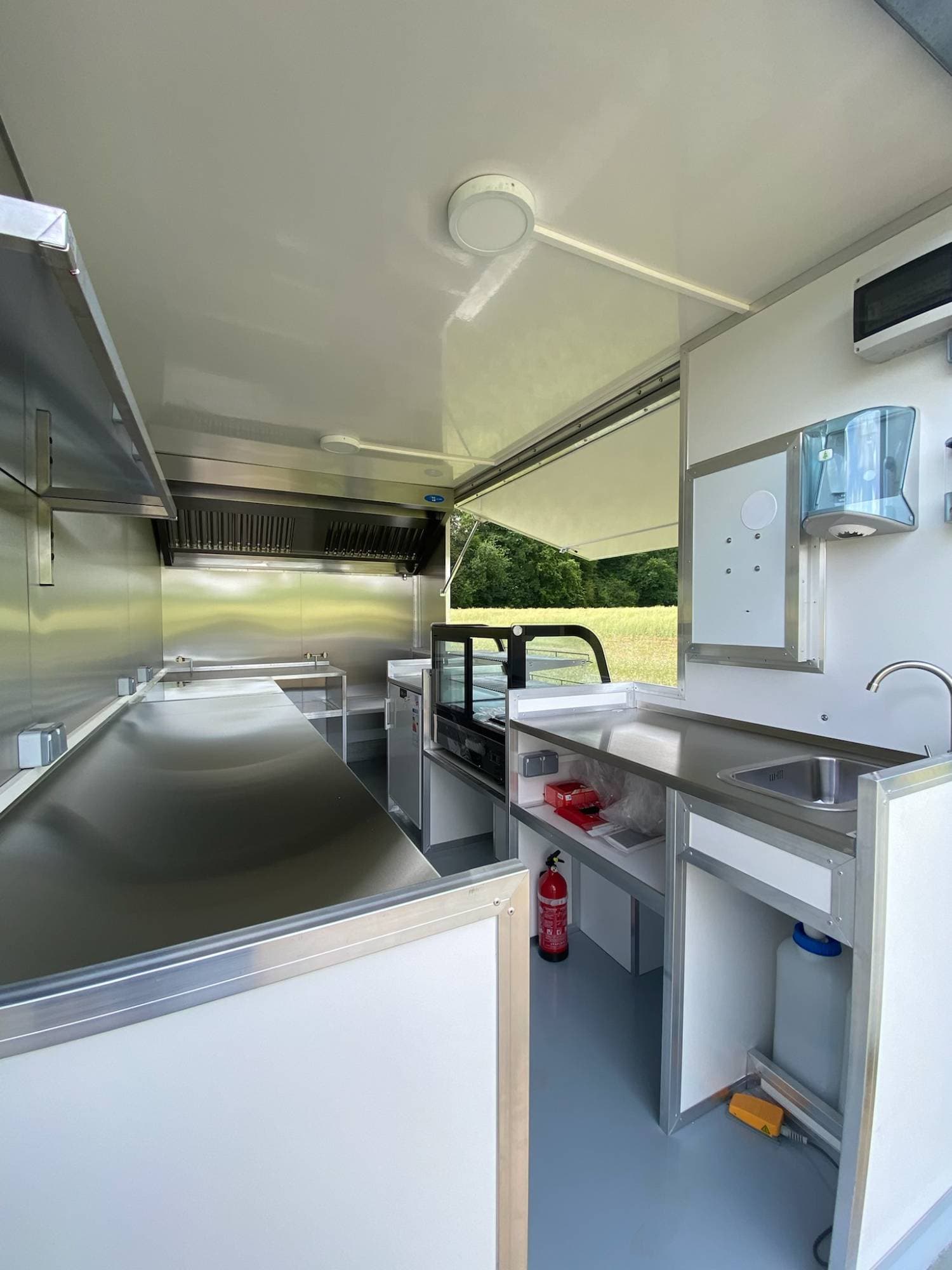Intérieur camion traiteur avec plans de travail inox, hotte aspirante, vitrine réfrigérée et évier professionnel