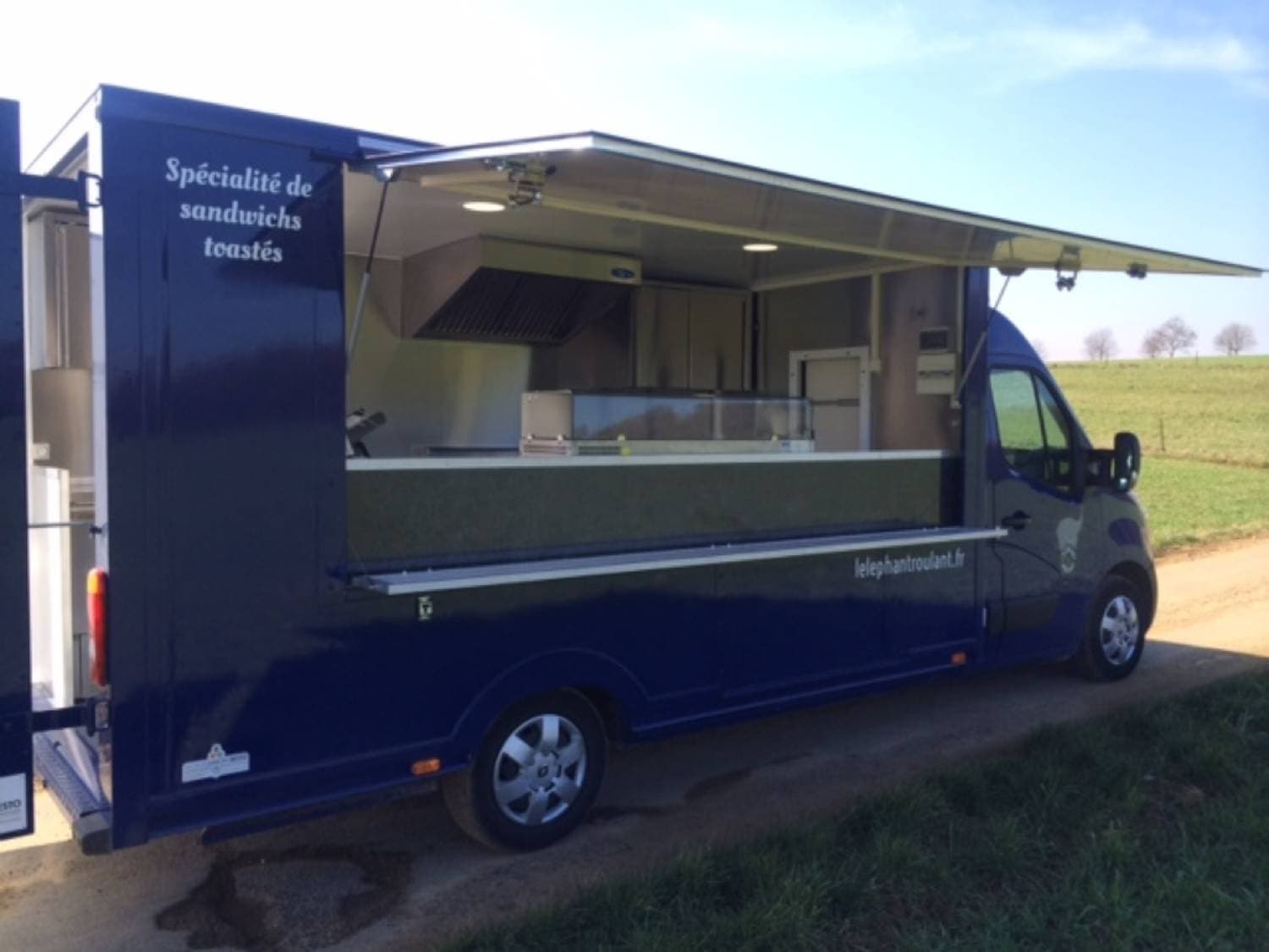 Food truck Renault Master bleu ouvert côté service, spécialité sandwichs toastés, cuisine professionnelle visible