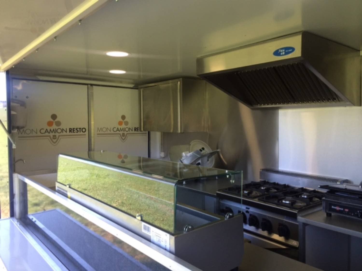 Intérieur food truck avec logo Mon Camion Resto, vitrine réfrigérée, plaques gaz et plans de travail inox