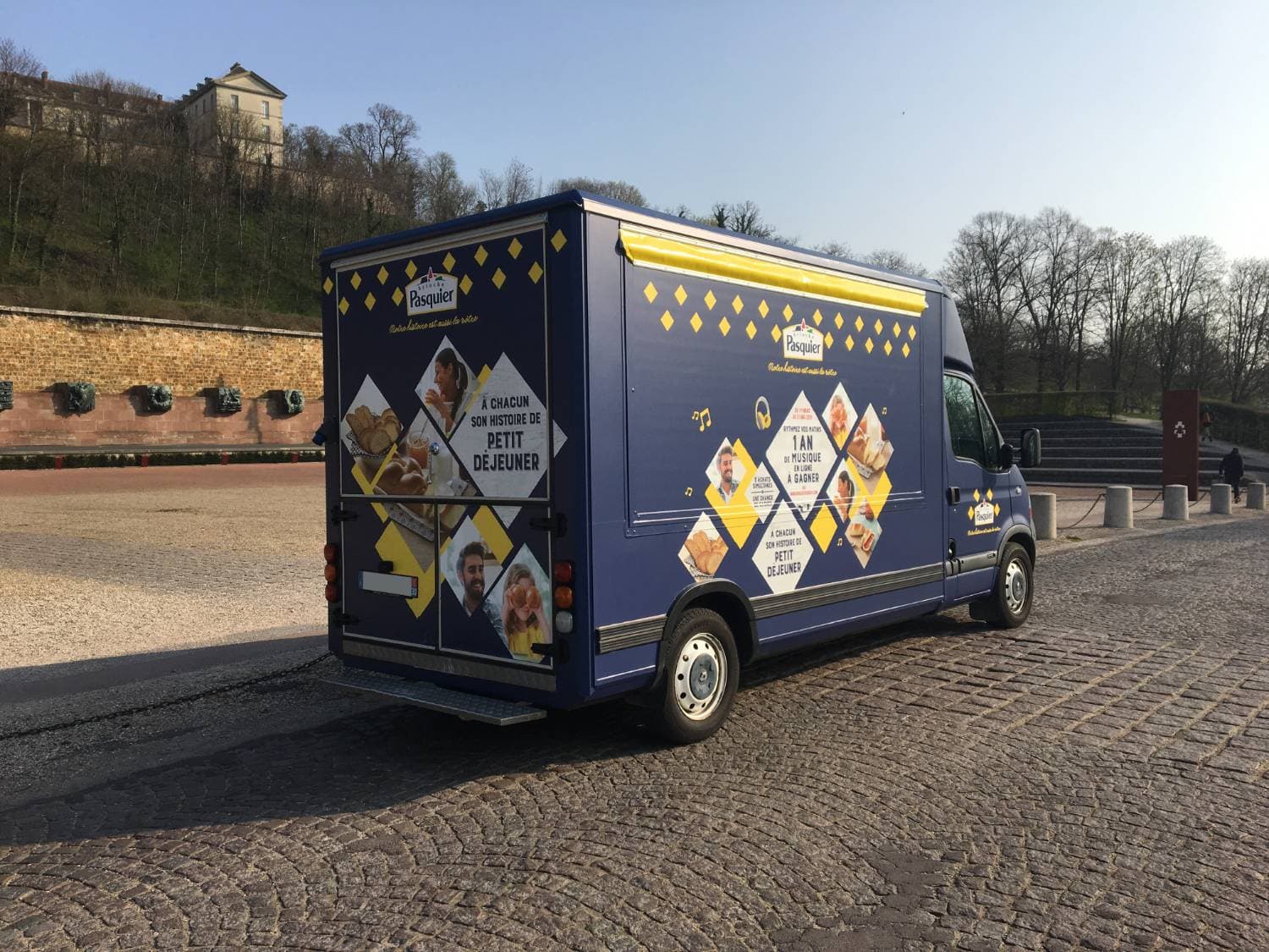 Food truck Brioche Pasquier vue arrière bleu et jaune avec losanges et photos de produits sur place pavée