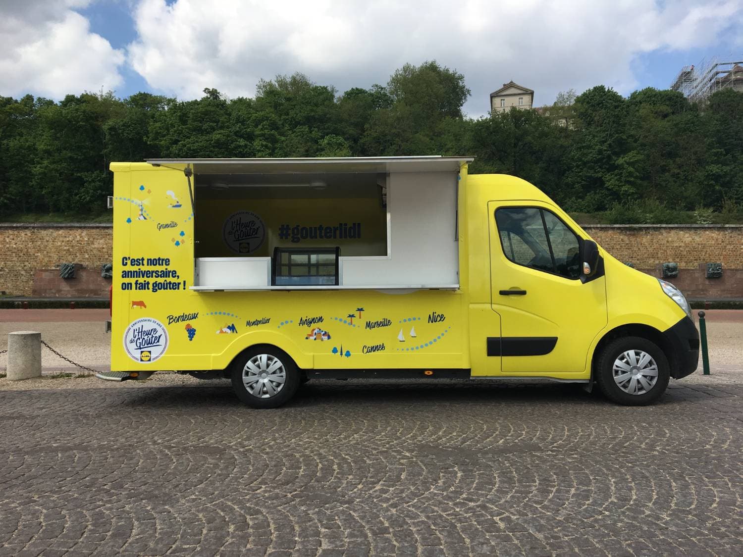 Food truck Lidl jaune volet ouvert avec comptoir et hashtag #gouterlidl sur place pavée ensoleillée