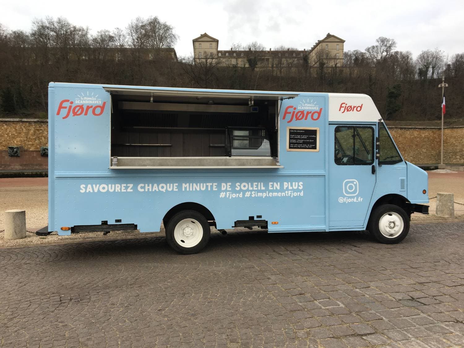 Step Van Fjord bleu ciel ouvert avec volet de service relevé, vue latérale droite sur place pavée