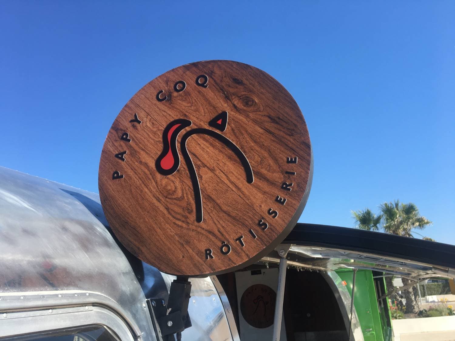 Enseigne artisanale en bois « Papy Coq Rôtisserie » sur le toit de l'Airstream