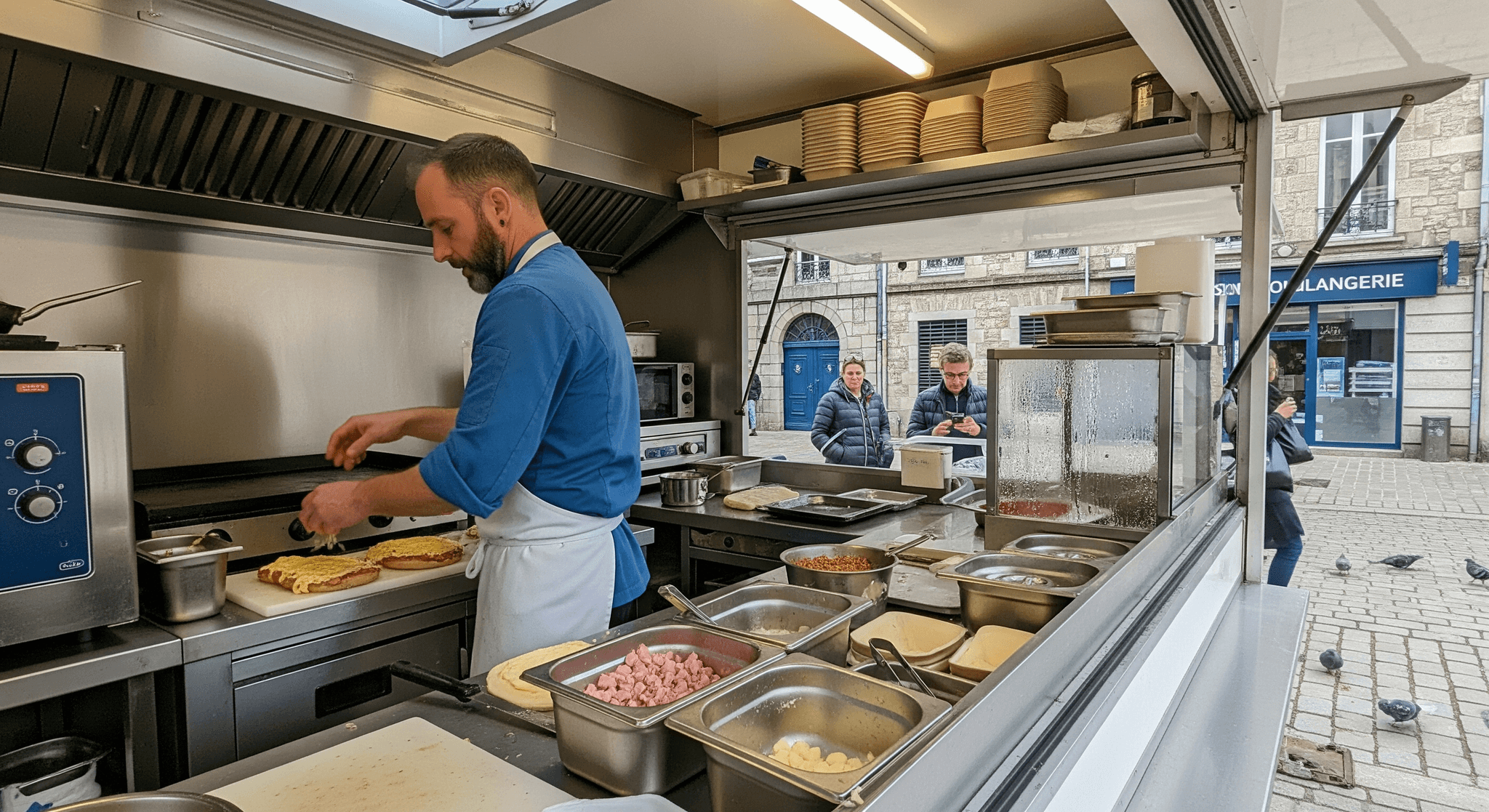 Chef préparant flamiche et welsh sur plancha inox dans un food truck Mon Camion Resto. Cuisine professionnelle aménagée.