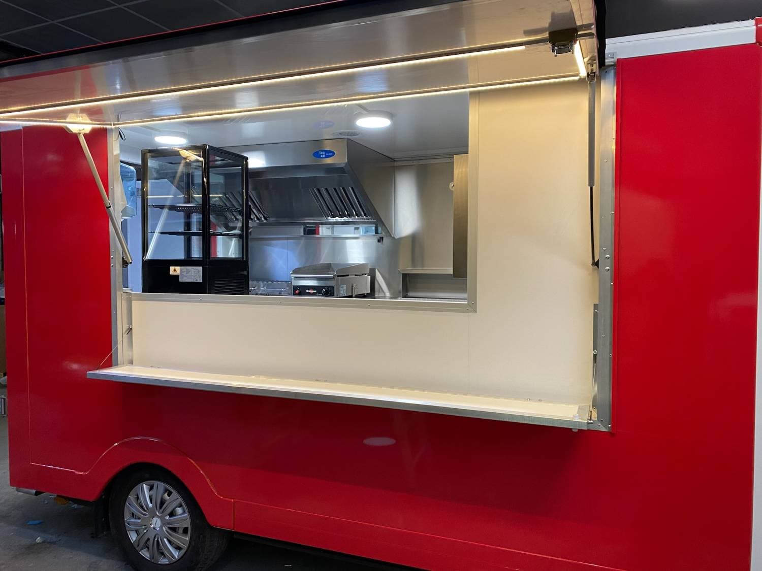 Camion pizza snack rouge ouvert en atelier avec vitrine d'exposition, plancha et hotte professionnelle éclairée