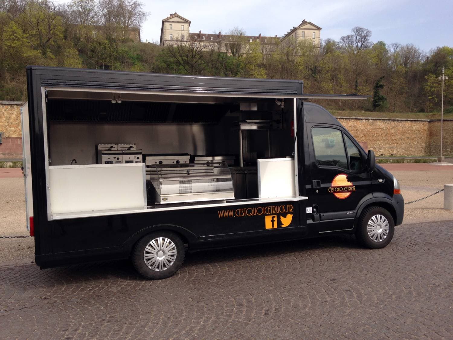 Food truck noir C'est Quoi Ce Truck ouvert avec cuisine visible, friteuse et plancha en inox