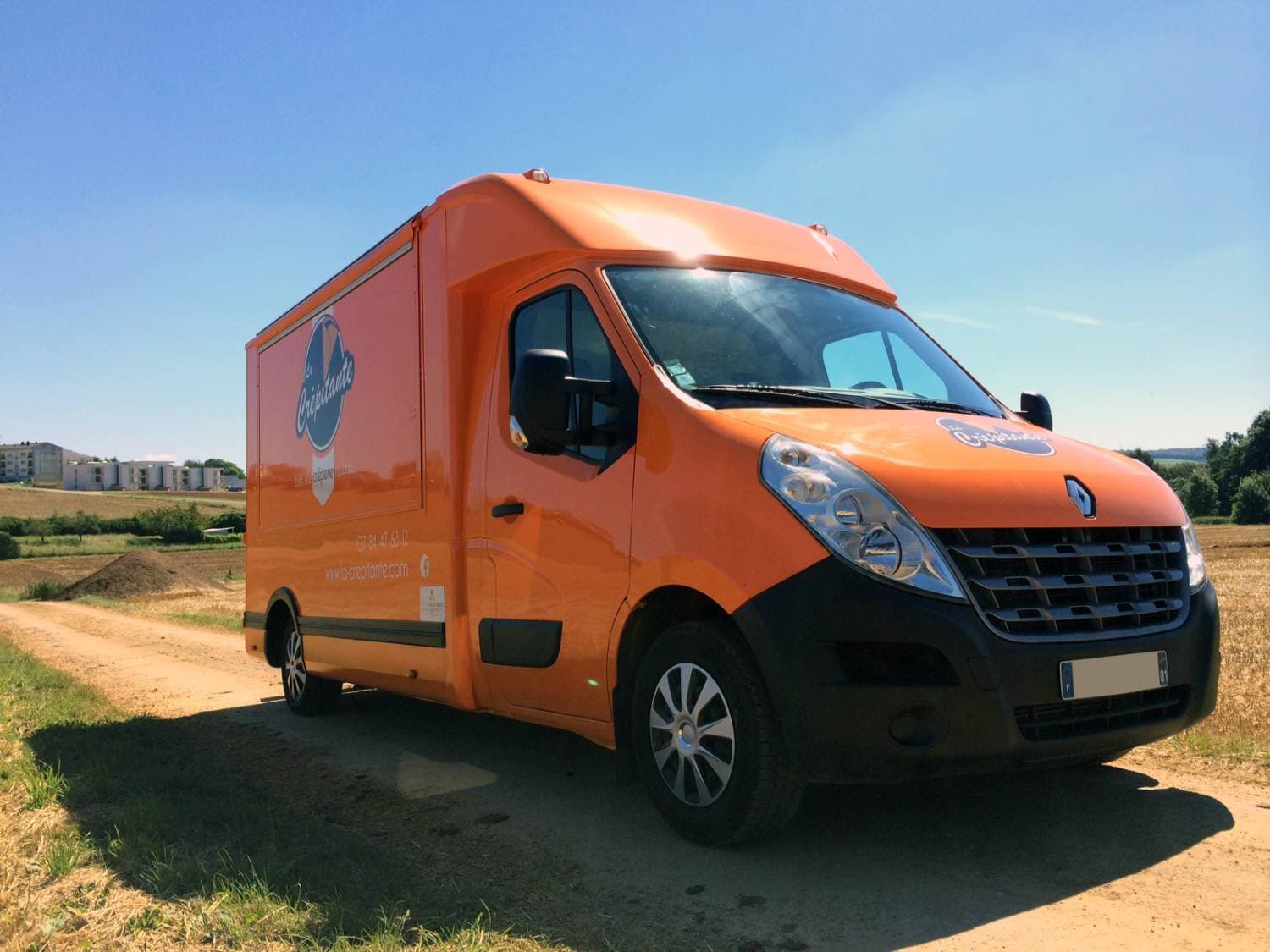 Renault Master orange La Crépitante vue trois-quarts avant dans un cadre champêtre ensoleillé