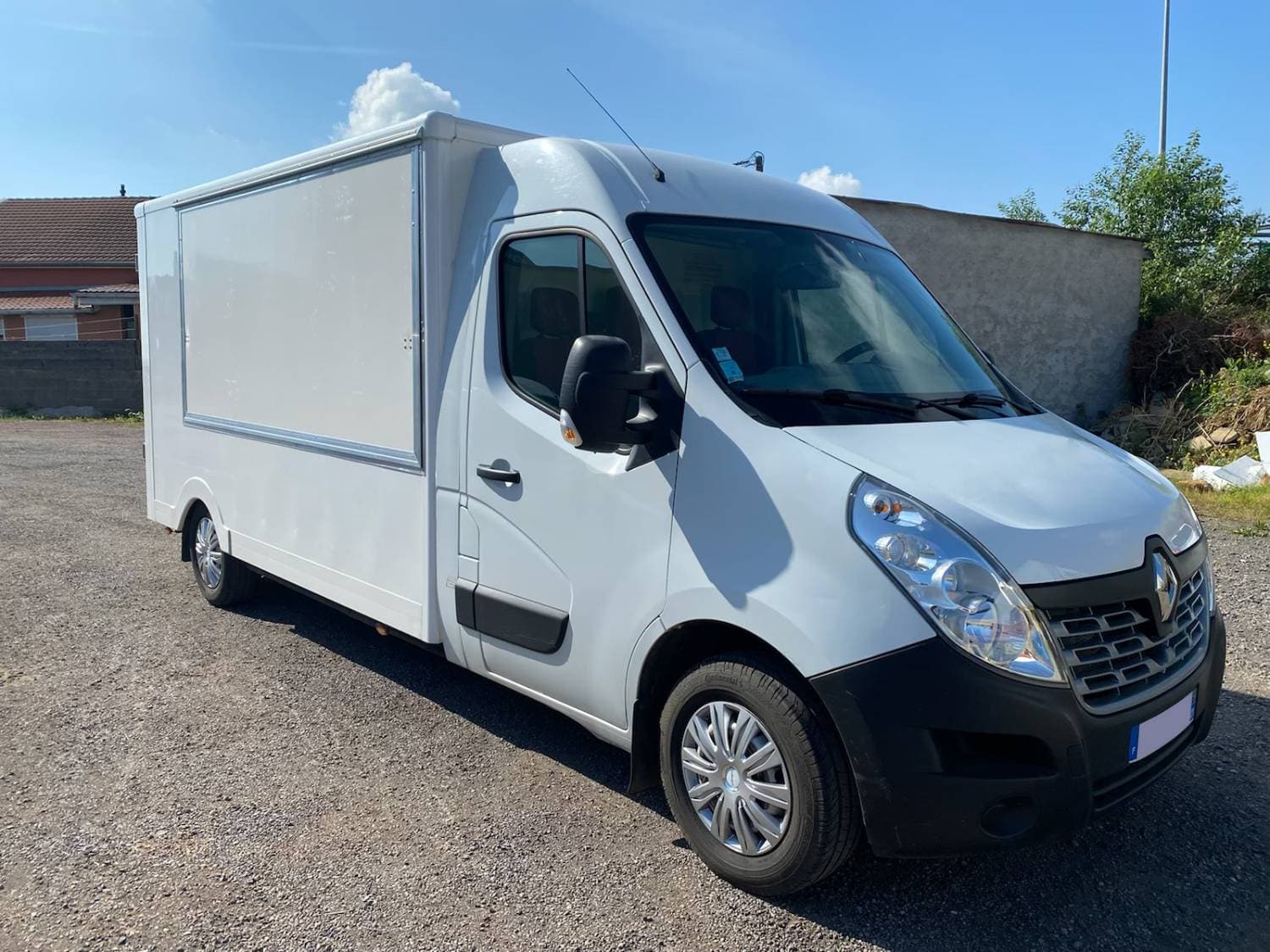 Camion cuisine blanc Renault Master avec volet de service fermé stationné sur terrain industriel