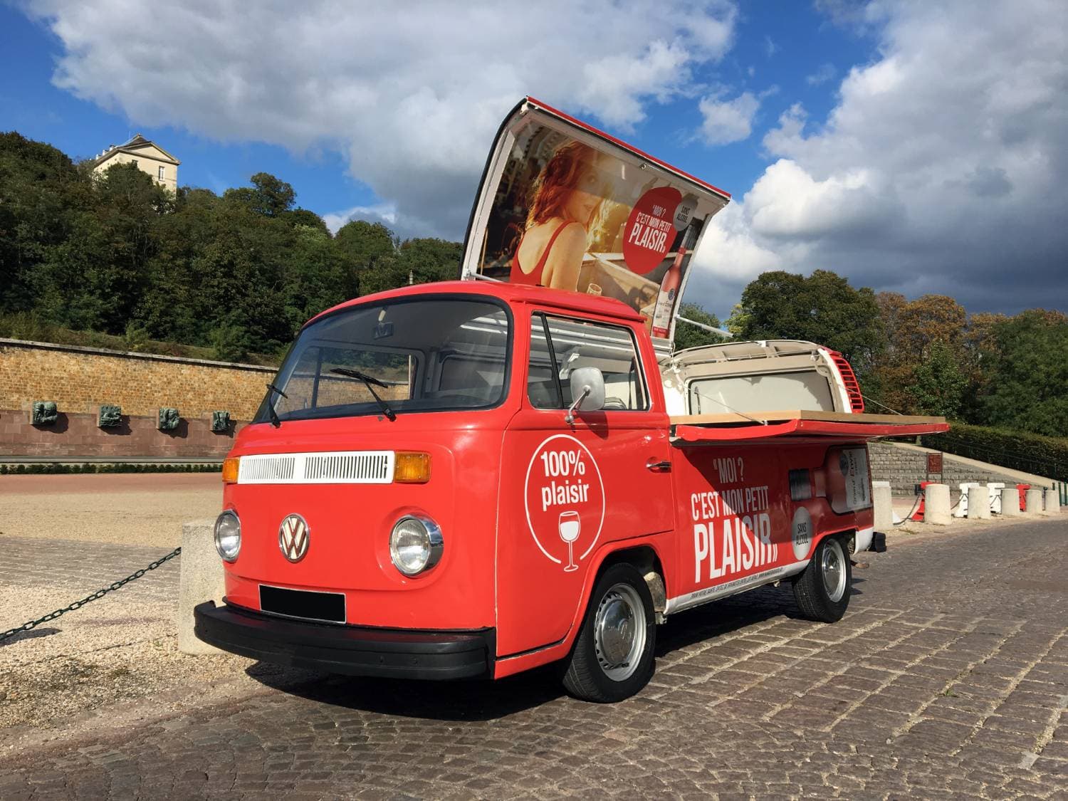 Combi VW pick-up rouge « 100% Plaisir » Grain d'Envie vu de face avec panneau publicitaire ouvert - roadshow promotionnel
