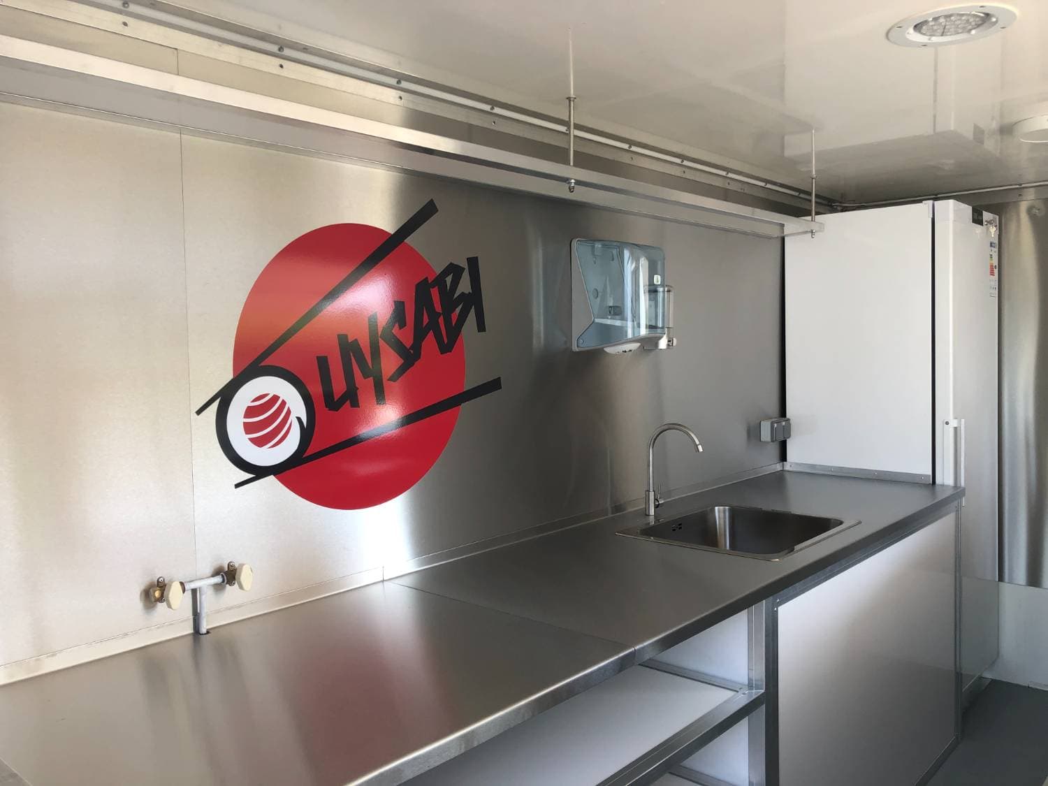 Intérieur inox du food truck Ouysabi avec logo rouge et noir, évier, plan de travail et distributeur essuie-mains