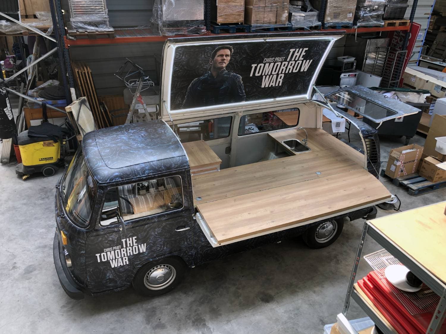 Combi VW pick-up avec total covering The Tomorrow War vu en plongée dans l'atelier - comptoir en bois et panneau lumineux